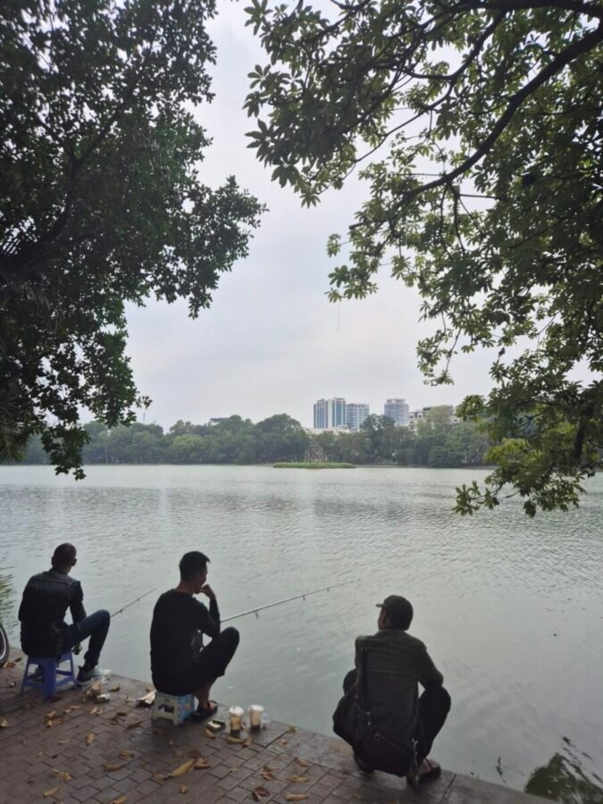 People sitting quietly by a lake in Hanoi surrounded by trees