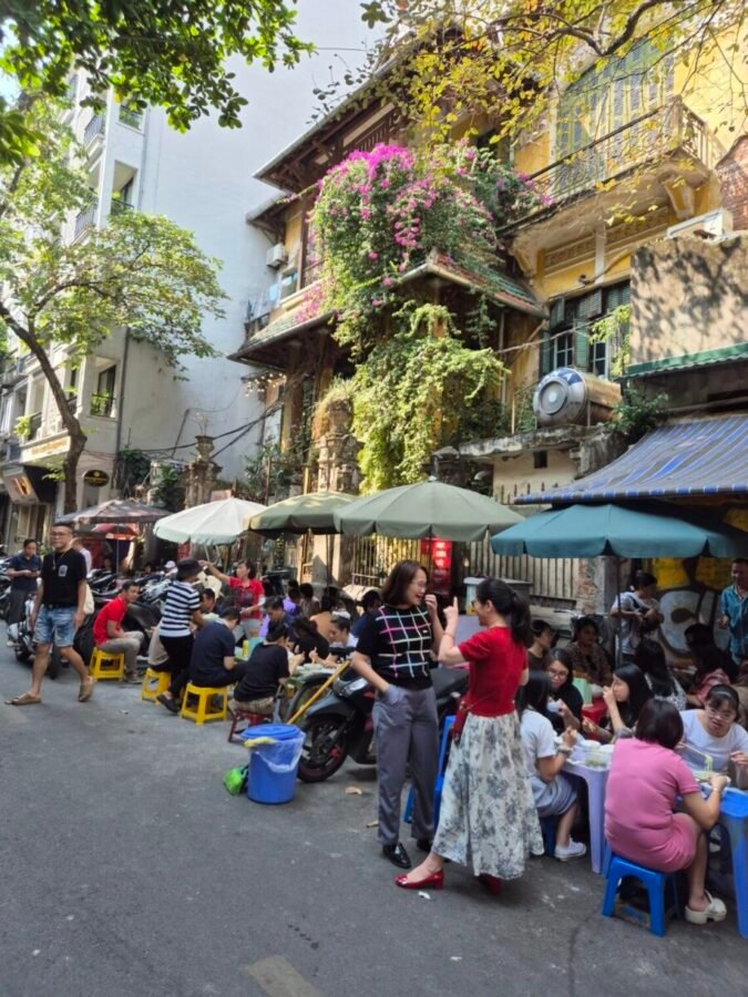 Street dining in Hanoi with people eating on low stools along a busy street