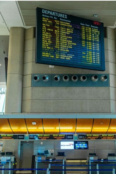 Airport departures board displaying flight schedules above airline check-in counters