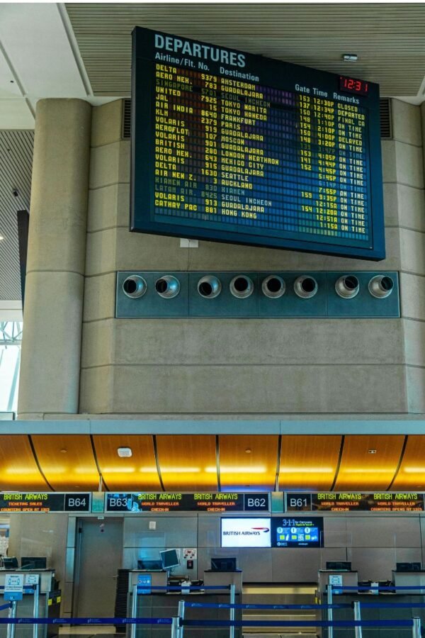 airport-departures-board-flight-schedule Airport departures board displaying flight schedules above airline check-in counters