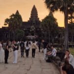 Angkor Wat at sunrise in Siem Reap with palm trees, temple silhouette, and visitors walking toward the entrance