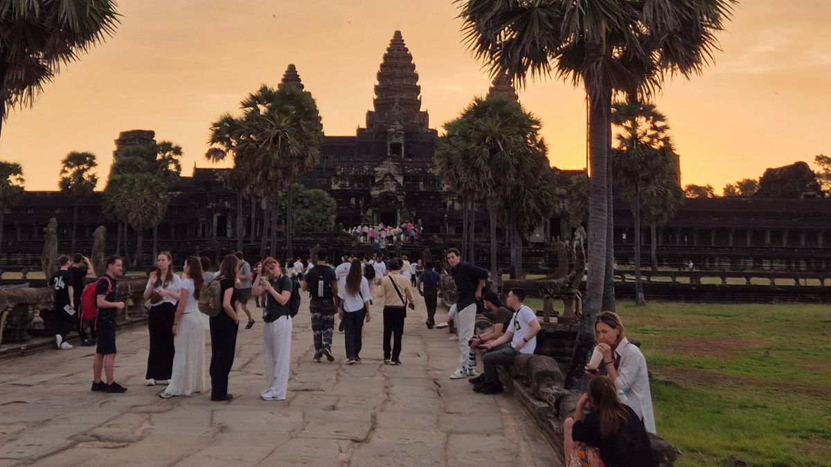 Angkor Wat at sunrise in Siem Reap with palm trees, temple silhouette, and visitors walking toward the entrance