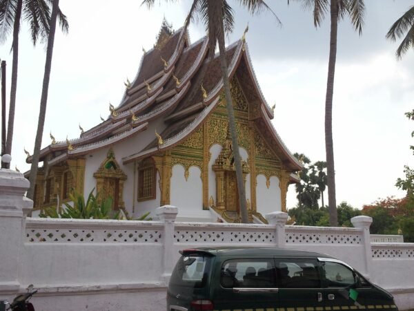 Traditional temple building in Luang Prabang viewed from the street with palm trees and a parked vehicle in front