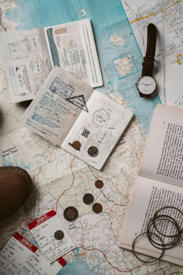 passport-boarding-passes-travel-map-flatlay Open passport with visa stamps, boarding passes, coins, and a watch placed on a travel map.