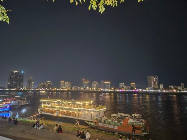 Phnom Penh skyline at night across the river with lit buildings and boats along the riverside