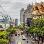 Busy daytime street traffic in Bangkok with cars, motorbikes and city buildings