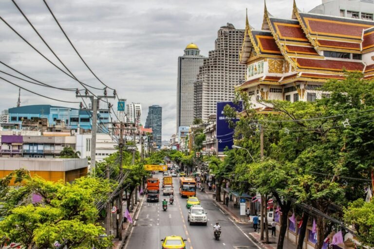 Busy daytime street traffic in Bangkok with cars, motorbikes and city buildings