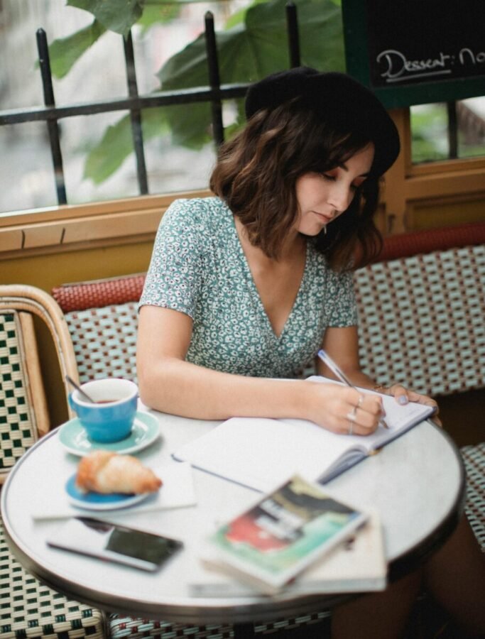 dining-alone-travel-journal-cafe Solo traveler writing in a journal at a café table with coffee and pastry