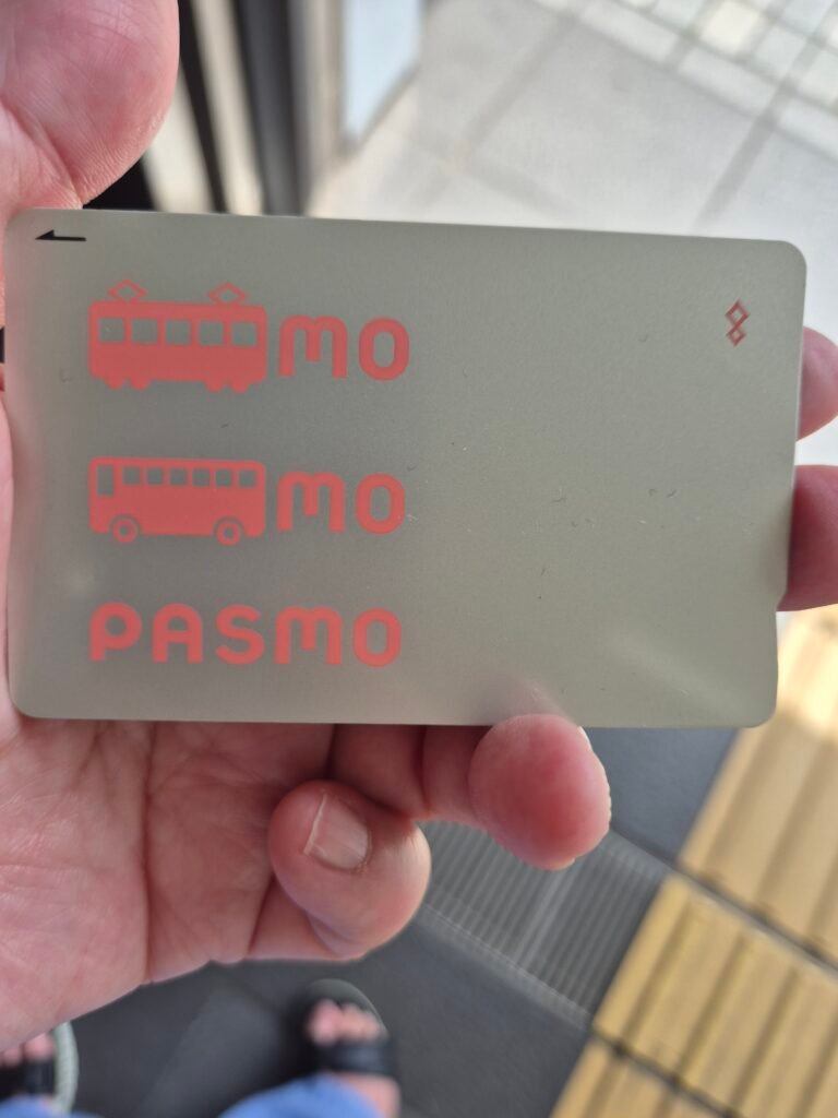 Close-up of a Pasmo transit card held in hand, showing the train and bus icons used across Japan