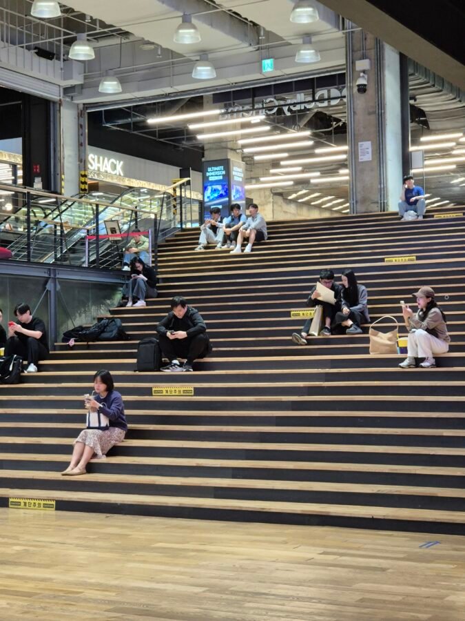 Wide stadium-style step seating at the Coex Mall cinema concourse in Seoul, with no proper seats — only bench-height steps used by people sitting and using their phones
