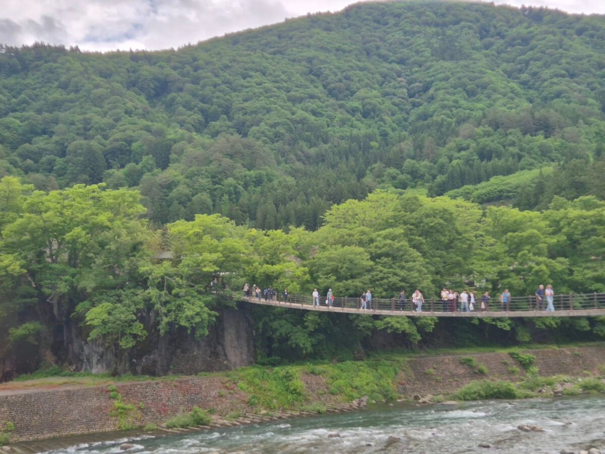deai-bridge-shirakawa-go-japan Visitors crossing Deai Bridge over the Shogawa River into Shirakawa-go, surrounded by forested mountains in Gifu Prefecture, Japan.