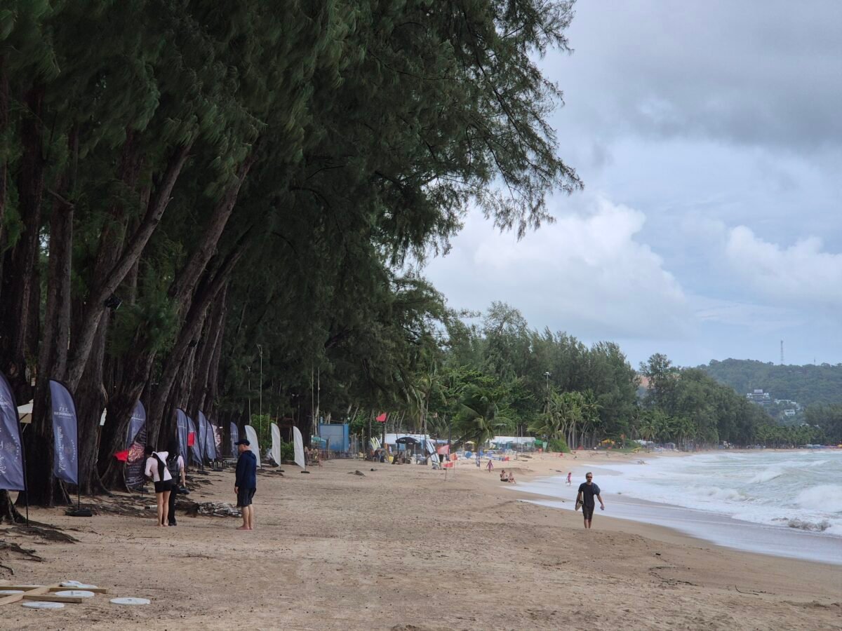 kamala-beach-phuket-overcast-quiet Kamala Beach, Phuket, under an overcast sky with rough surf, and casuarina trees lining the quiet northern stretch of sand.