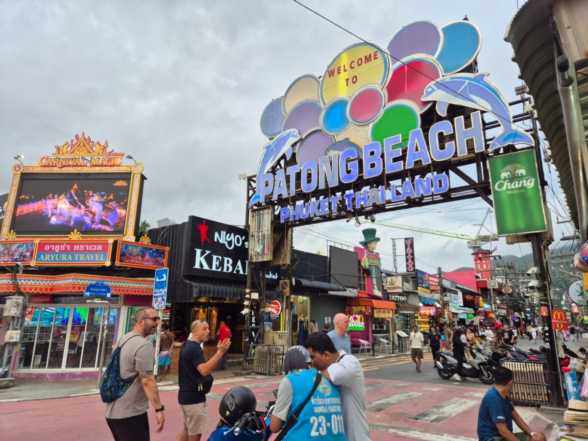 patong-beach-welcome-sign-shops The "Welcome to Patong Beach" arch on Bangla Road, Phuket, surrounded by bars, tattoo shops, and street signage.