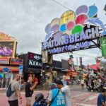 The "Welcome to Patong Beach" arch on Bangla Road, Phuket, surrounded by bars, tattoo shops, and street signage.