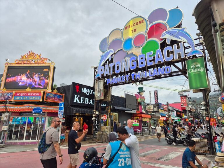 The "Welcome to Patong Beach" arch on Bangla Road, Phuket, surrounded by bars, tattoo shops, and street signage.